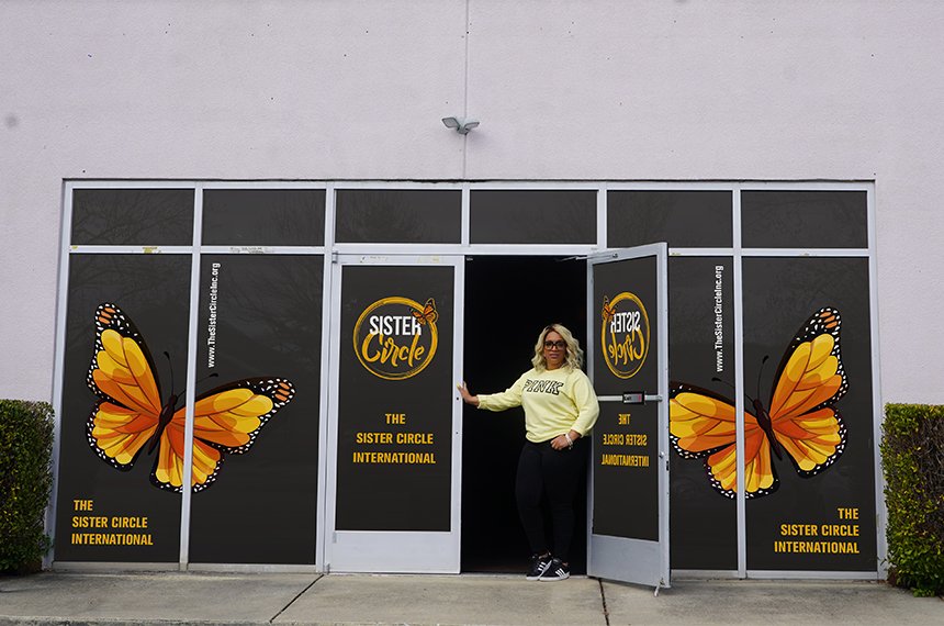 Storefront window wrap with monarch butterflies and Sister Circle logo; founder stands in open doorway, design by Rahat Abir.